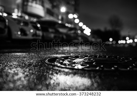 Rainy night in the big city, the light from the lanterns in the courtyard of the house in which the parked cars. View from the hatch at the level of the pavement, in black and white tones