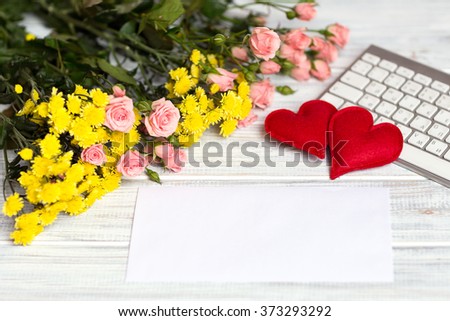 envelope lying on a wite textural table next to a bouquet of pink  small roses and keyboard with two hand made hearts
