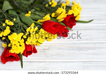 bouquet of yellow flowers and red tulips lying on a white textured table