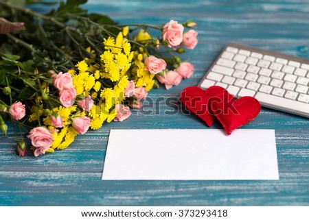envelope lying on a blue textural table next to a bouquet of pink  small roses and keyboard with two hand made hearts