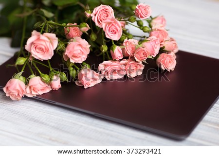 bouquet of small pink roses lying on a blue textured table next to laptop