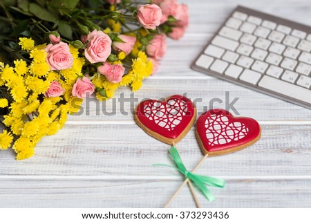 phone lying on a wite textural table next to a bouquet of pink  small roses and keyboard with two hand made hearts
