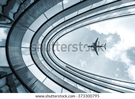 Low view blue colorized picture of modern architecture building with landing airplane in background 