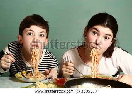 happy teen siblings boy and girl eat spaghetti together hanging from mouth grimacing happily