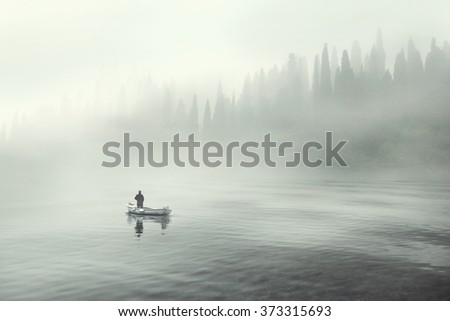 Man fishing on a boat in a mystic foggy lake Royalty-Free Stock Photo #373315693