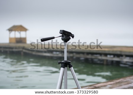 Camera tripod. Photo was taken outdoor in a park, near lake. It was very early in the morning, with fog all around photo stand.