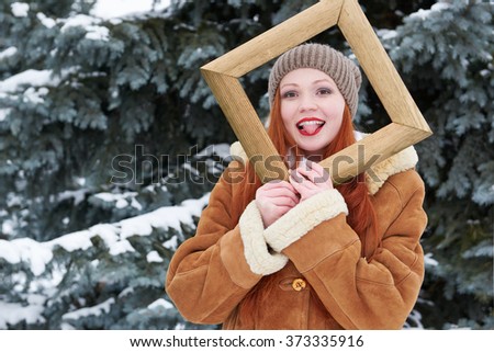 Woman portrait in wooden photo frame at winter season. Snowy weather in fir tree forest.