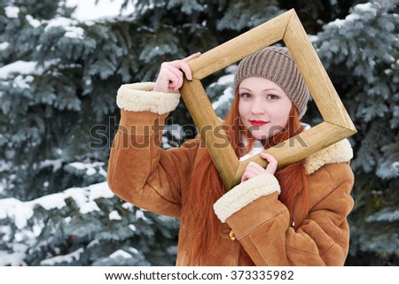 Girl portrait in wooden photo frame at winter season. Snowy weather in fir tree forest.