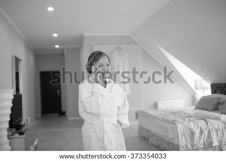 Beautiful bride talking via phone to groom while getting ready at hotel room. Bridal happy moments. Wedding picture in black and white. 