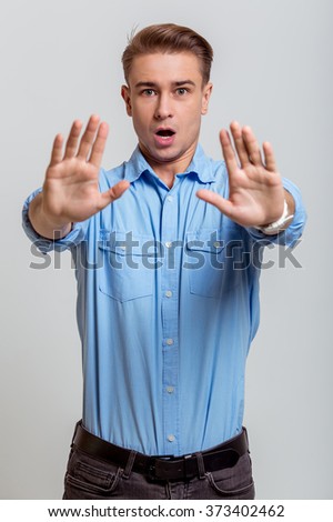 Portrait of attractive young blond businessman in blue shirt looking in camera, warning and showing his palms, standing against gray background