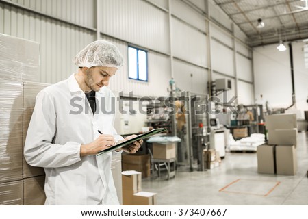 Worker In warehouse for food packaging. Manager writing on clipboard in automated production line at modern factory. Color toned image.