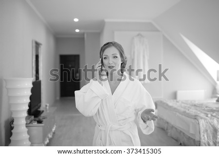 Beautiful bride talking via phone to groom while getting ready at hotel room. Bridal happy moments. Wedding picture in black and white. 