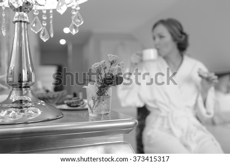 Young bride having quick snack while getting ready at hotel room. Bridal happy moments. Wedding picture in black and white. 