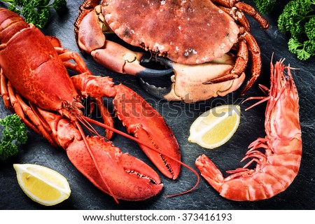 Fine selection of crustacean for dinner. Lobster, crab and jumbo shrimp on dark background  Royalty-Free Stock Photo #373416193