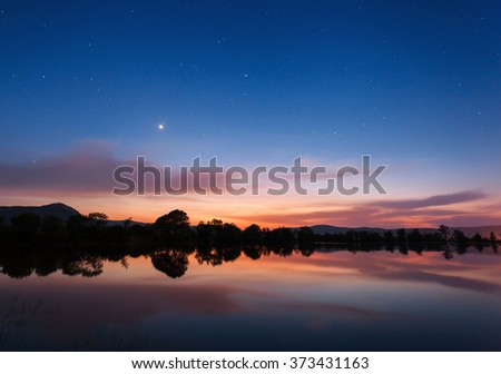 Beautiful night landscape on the mountain lake with stars and reflected clouds in water in spring. Colorful sky. Nature background 
