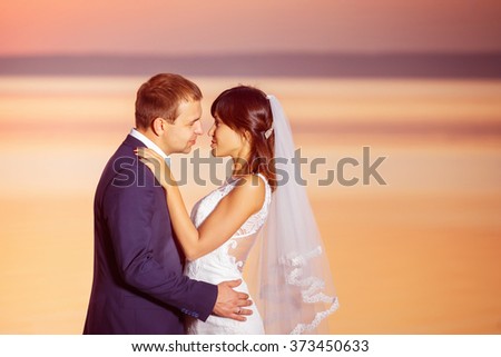 Beautiful happy couple is embracing at golden summer sea sunset background.