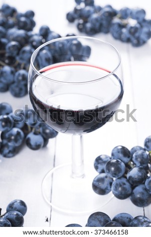 glass of red wine and blue grapes on white wooden table background