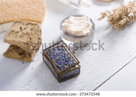 moisturizer, organic soap, henna blocks, dropper, sponge, and dried lavenders on white wood table background