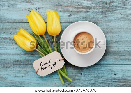 Coffee mug with yellow tulip flowers and notes good morning on blue rustic table from above, breakfast on Mothers day or Womens day