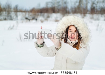 Girl taking selfie. Christmas girl outdoor self portrait. Woman in winter clothes on a snow field.