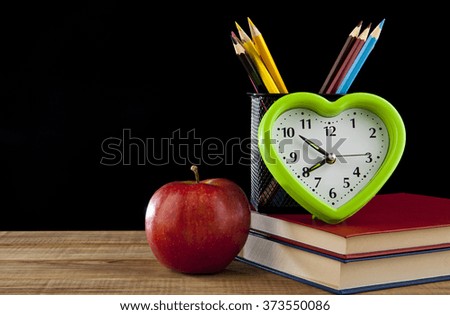 Apple, pencils, books and clock on black background