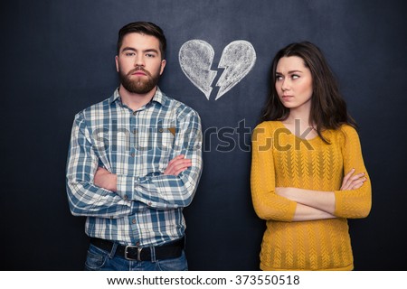 Portrait of young couple after argument standing separately with hands folded over blackboard background Royalty-Free Stock Photo #373550518