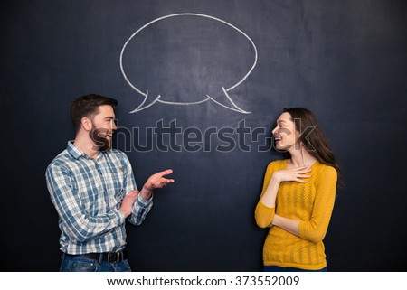 Happy young couple talking over chalkboard background with drawn empty dialogue Royalty-Free Stock Photo #373552009