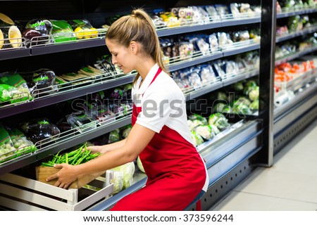 Female worker putting vegetable box in shelf in grocery store