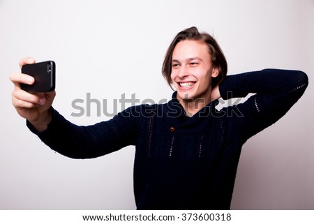 Selfie time! Smile young man in black sweater holding mobile phone and making photo of himself while standing against white background