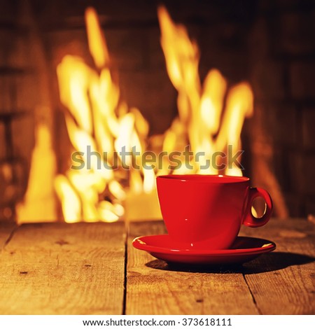 Red cup of coffee or tea on wooden table near  fireplace. Winter and Christmas holiday concept. Photo with retro filter effect.