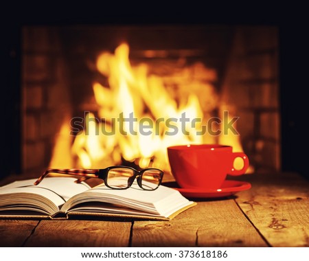 Red cup of coffee or tea, glasses and old book on wooden table near fireplace. Winter and Christmas holiday concept. Photo with retro filter effect.