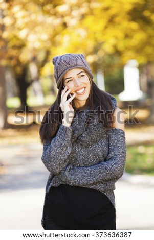 Beautiful woman walking in autumn park. Fall season. Woman talking on the phone
