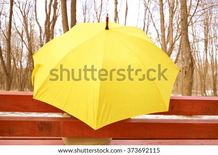 Young beautiful girl sitting alone under umbrella on a bench in the park in autumn. Golden autumn