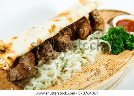 Beautiful juicy kebab in lavash with onion and herbs on wooden background