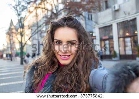 Smiling woman taking a selfie photo in an urban street in winter