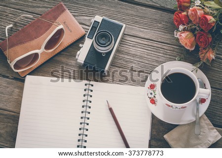 Vintage Film Look: cup of coffee with camera and notebook on wooden boards abstract background