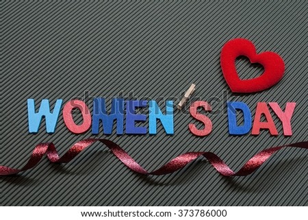 Women's day text wooden letters with heart and red ribbon . Isolate on small stripes of grey color paper texture background.