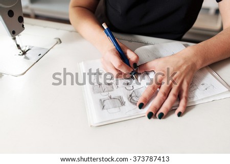 Seamstress creates a sketch in the working notebook. designer draws the clothes and bags. Royalty-Free Stock Photo #373787413