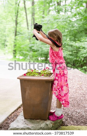 Young girl in a colorful dress using a camera.  Finding creative and unique perspectives on her subject.  Concepts could include childhood, imagination, creativity, experimentation, or several others.