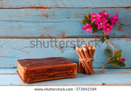 vintage notebook and stack of wooden colorful pencils on wooden texture table next to purple bougainvillea flower. vintage filtered
