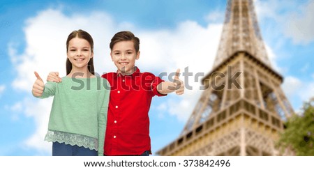 childhood, travel, tourism, gesture and people concept - happy smiling boy and girl hugging and showing thumbs up over paris eiffel tower background