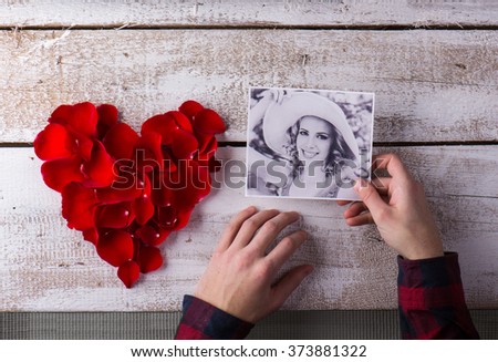 Mans hands holding his girlfriends photo. Red rose petal heart.