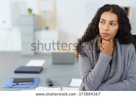 businesswoman with hand on chin sitting at desk in the office in thoughts Royalty-Free Stock Photo #373884367