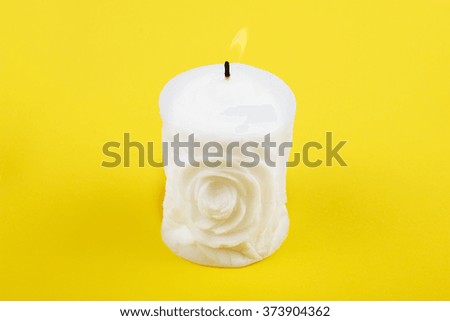 Carved white candle on yellow background. Souvenir gift candle in the shape of rose. Candle lit. St. valentine's day. 