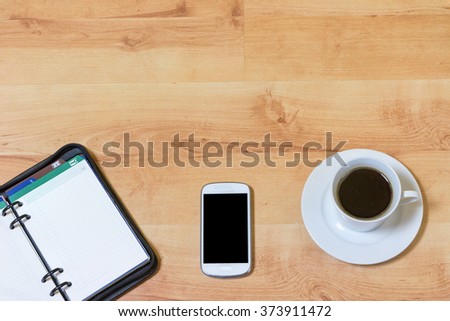 Smart phone, cup of coffee and manager diary are lying in the bottom half of the wooden table. In the upper half of the picture is the place for your text. All potential trademarks are removed.