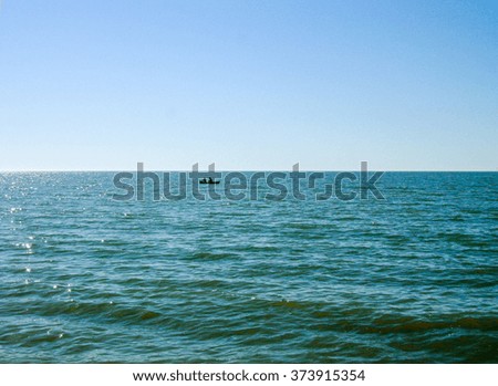 A calm sea, and the silhouettes of small boat and two fishermen are far away.