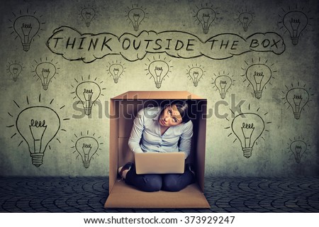 Think outside the box concept. Young woman sitting inside box using working on laptop computer isolated on gray office wall background 