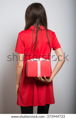 bcute girl hides behind a red gift on a grey background
