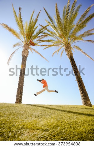 Joyful jumping excited photographer on the palm tree, green grass and blue sky background