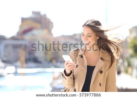 Happy beautiful woman walking and writing or reading sms messages on line on a smart phone while the wind moves her hair in a street of a port Royalty-Free Stock Photo #373977886